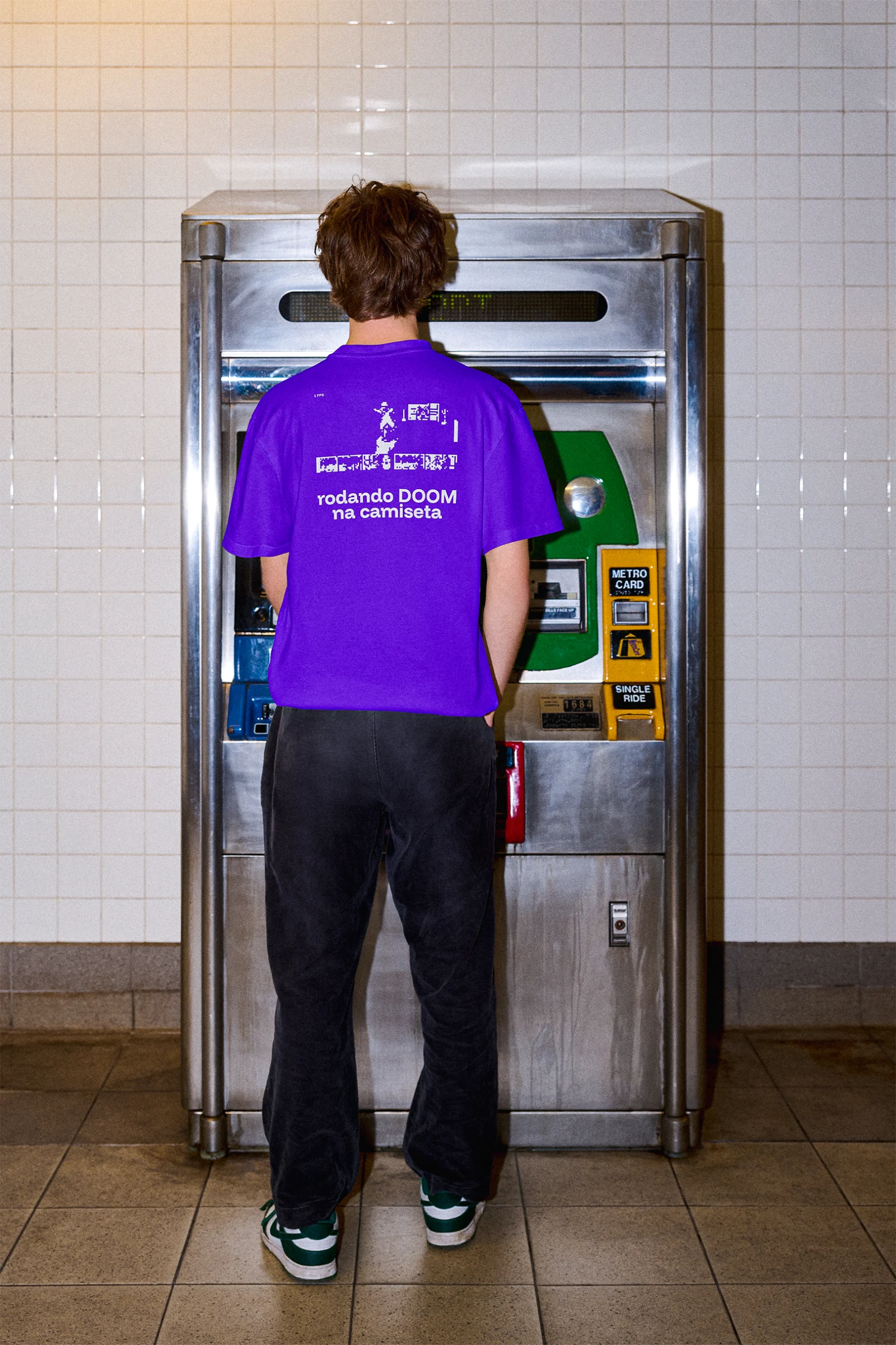 Camiseta roxa com estampa em pixel, vista de costas em uma máquina de metrô.
